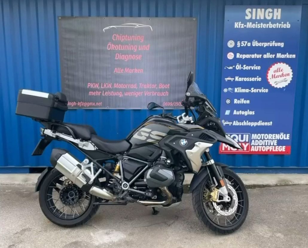 BMW R 1250 GS mit Topcase vor dem Werkstatt-Banner des KFZ-Meisterbetriebs Singh